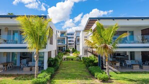A modern hotel with two-story buildings, outdoor seating areas, and palm trees. - O'Biches by Horizon Holidays (Trou aux Biches)