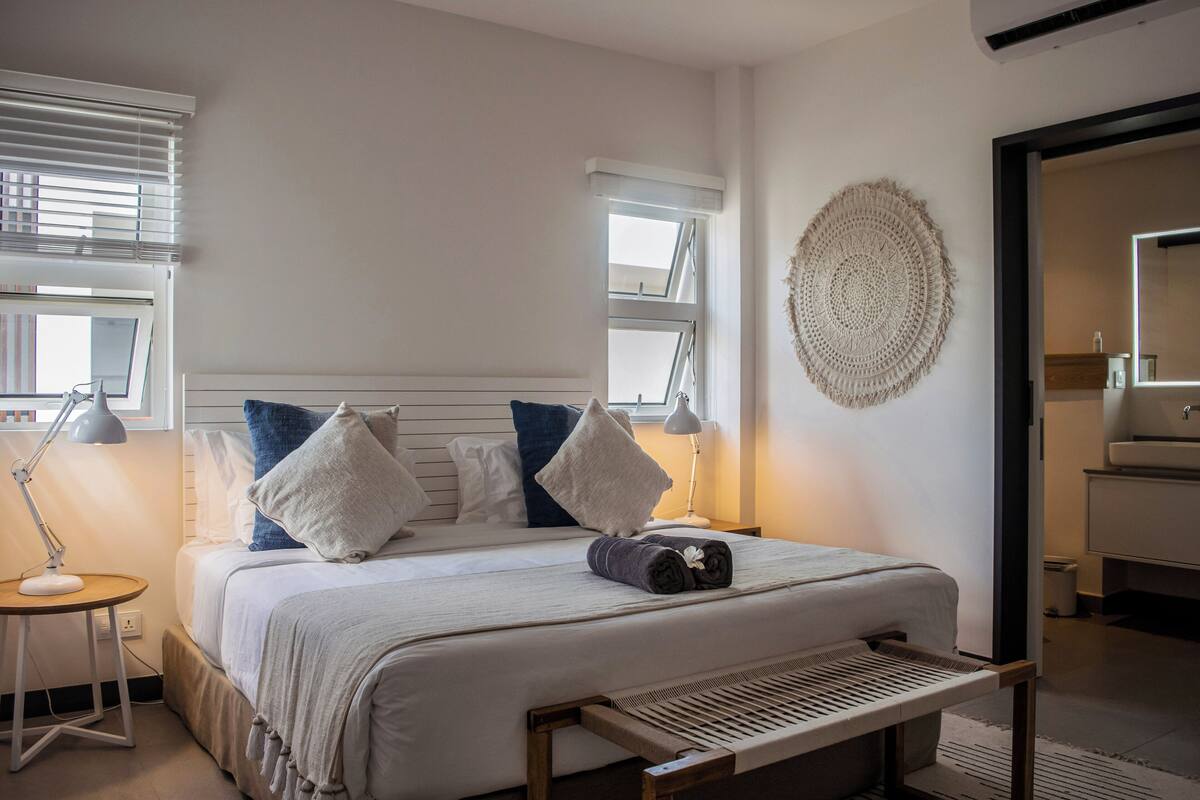 A neatly made bed with pillows, a bedside lamp, and a wall hanging.