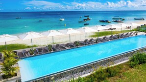 A swimming pool with lounge chairs and umbrellas, a beach with boats, and a clear blue sky. - O'Biches by Horizon Holidays (Trou aux Biches)