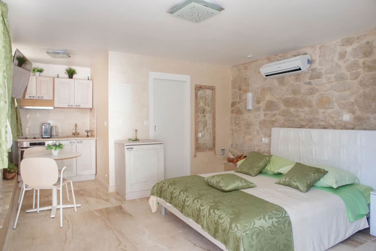 A bedroom with a bed, green pillows, a white headboard, and a stone wall.