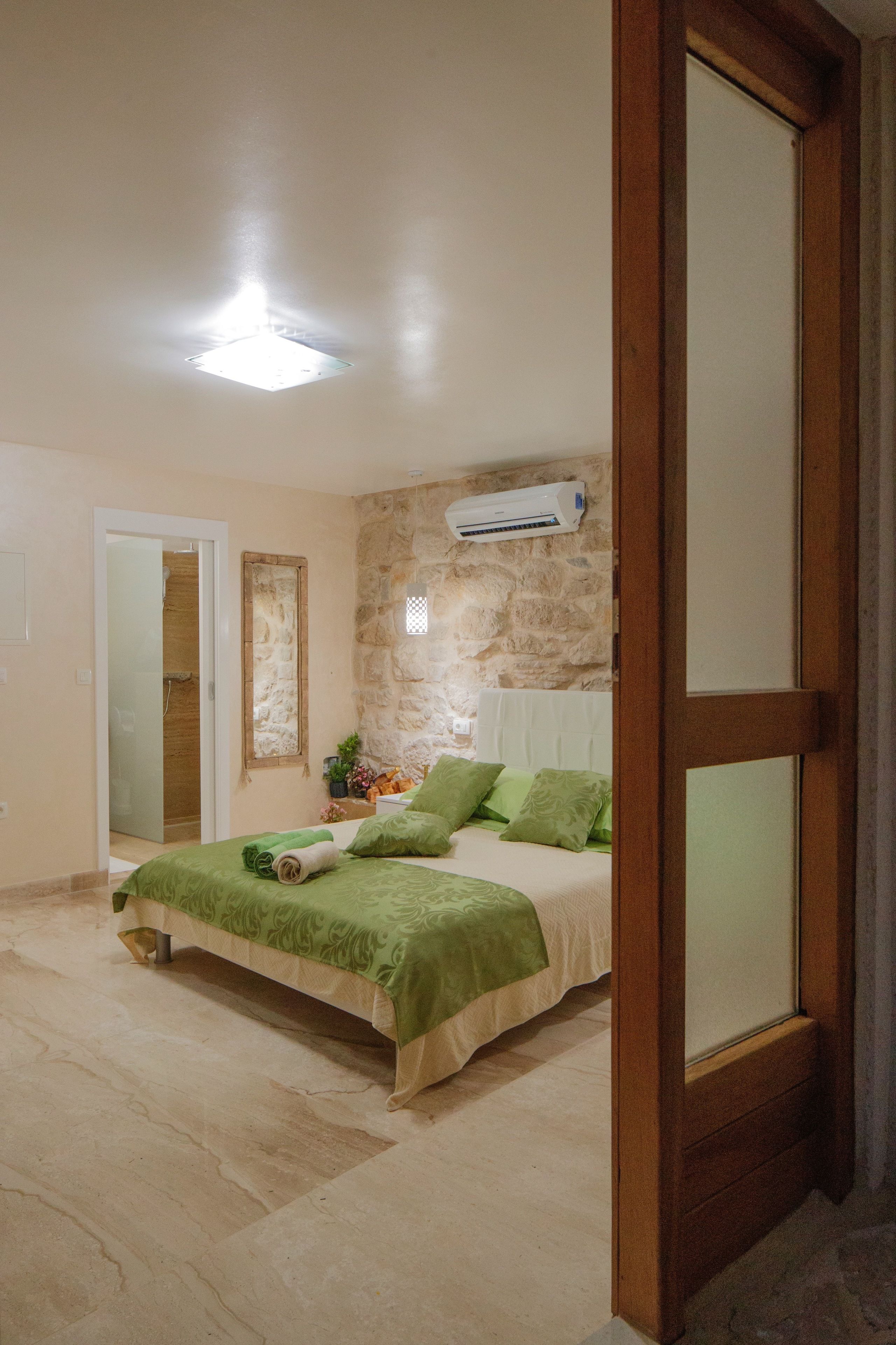 Un dormitorio con pared de piedra, cama con ropa de cama verde, puerta de madera y una lámpara en el techo.