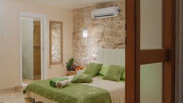 Un dormitorio con pared de piedra, cama con ropa de cama verde, puerta de madera y una lámpara en el techo.