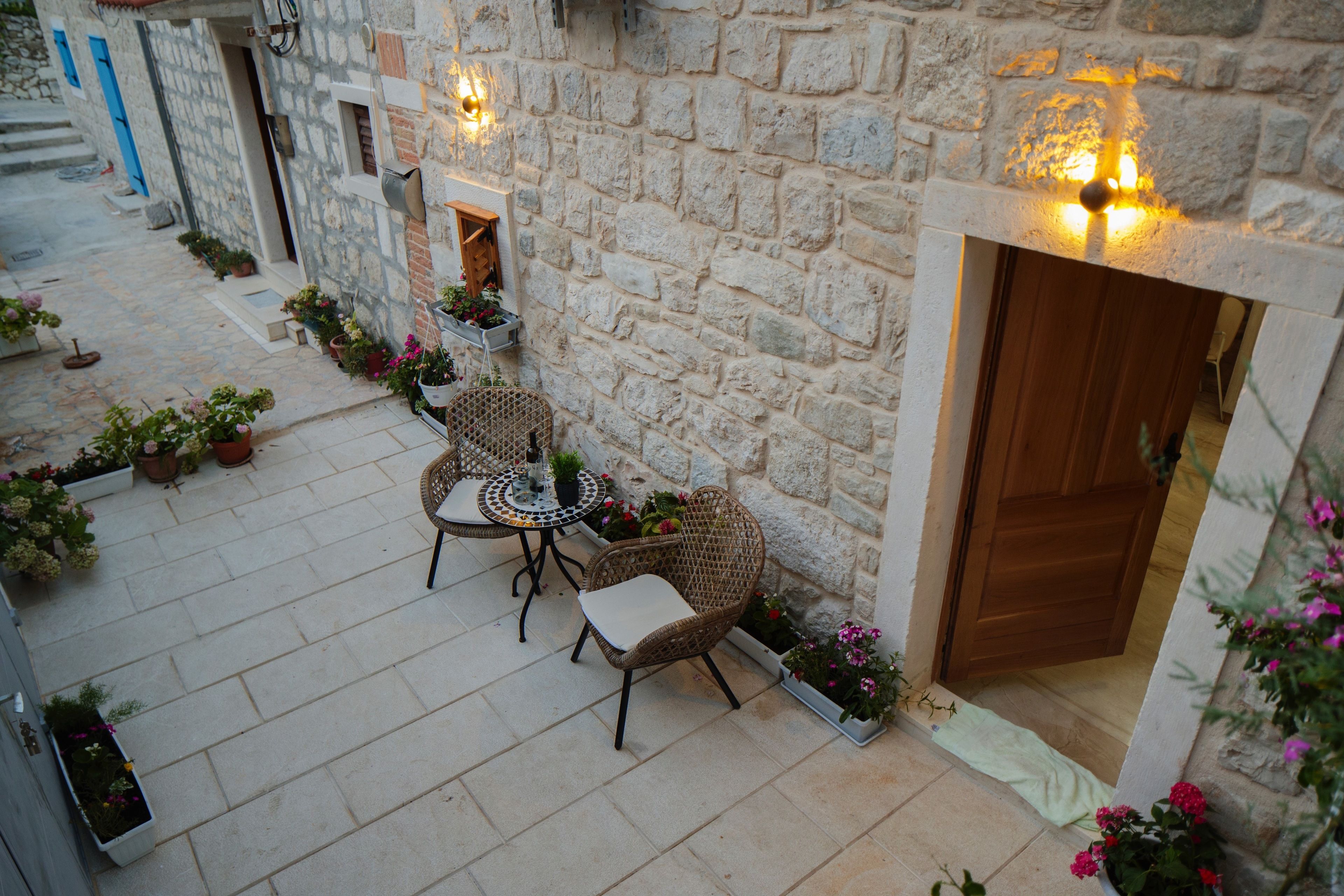 A stone courtyard with a table and chairs, potted plants, and a wooden door.