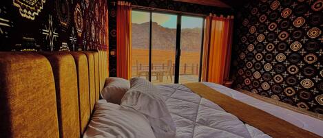 A room with a large bed, a view of mountains through a sliding door, patterned walls, and a wooden ceiling.
