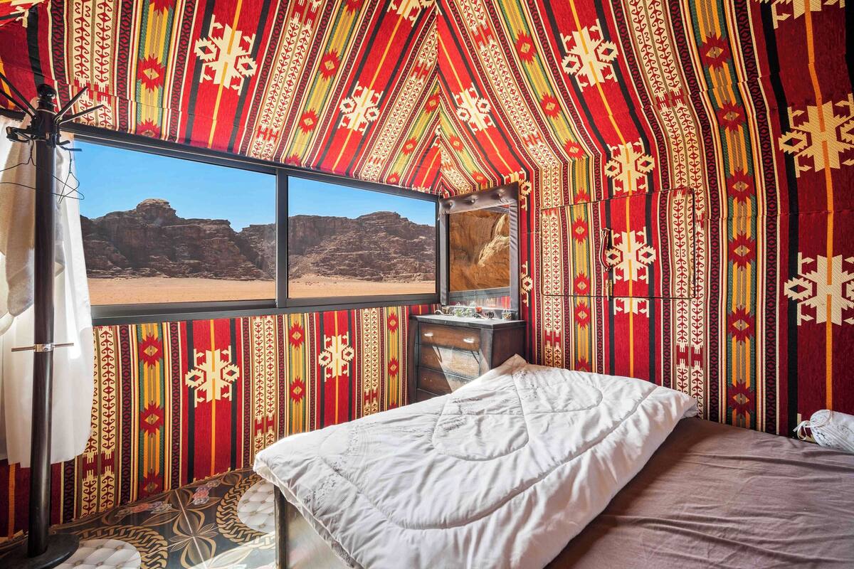 Una habitación con un ventanal grande, una cama y una mesita.