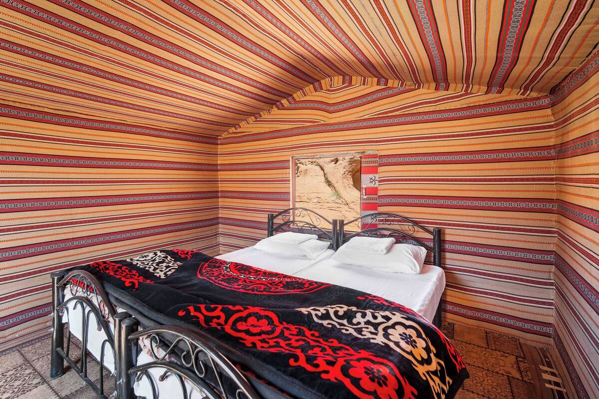 Una habitación con papel tapiz a rayas, una cama con colcha de diseño negro y rojo, y un cuadro en la pared.