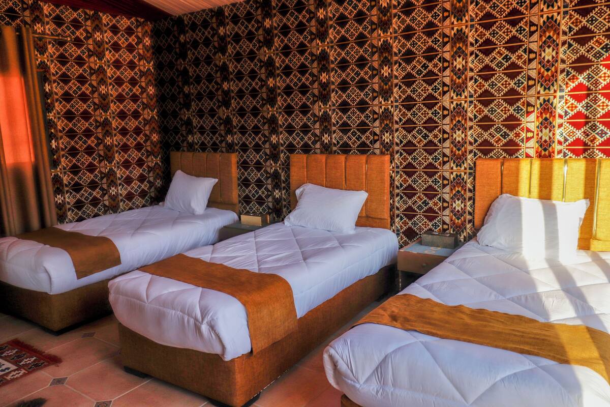 Habitación de hotel con tres camas, papel tapiz estampado y una paleta de colores cálidos.
