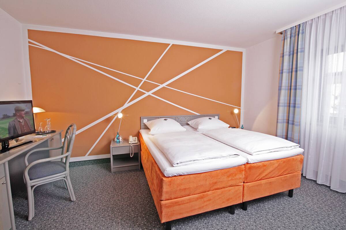 A hotel room with a bed, a desk, a chair, and a television.
