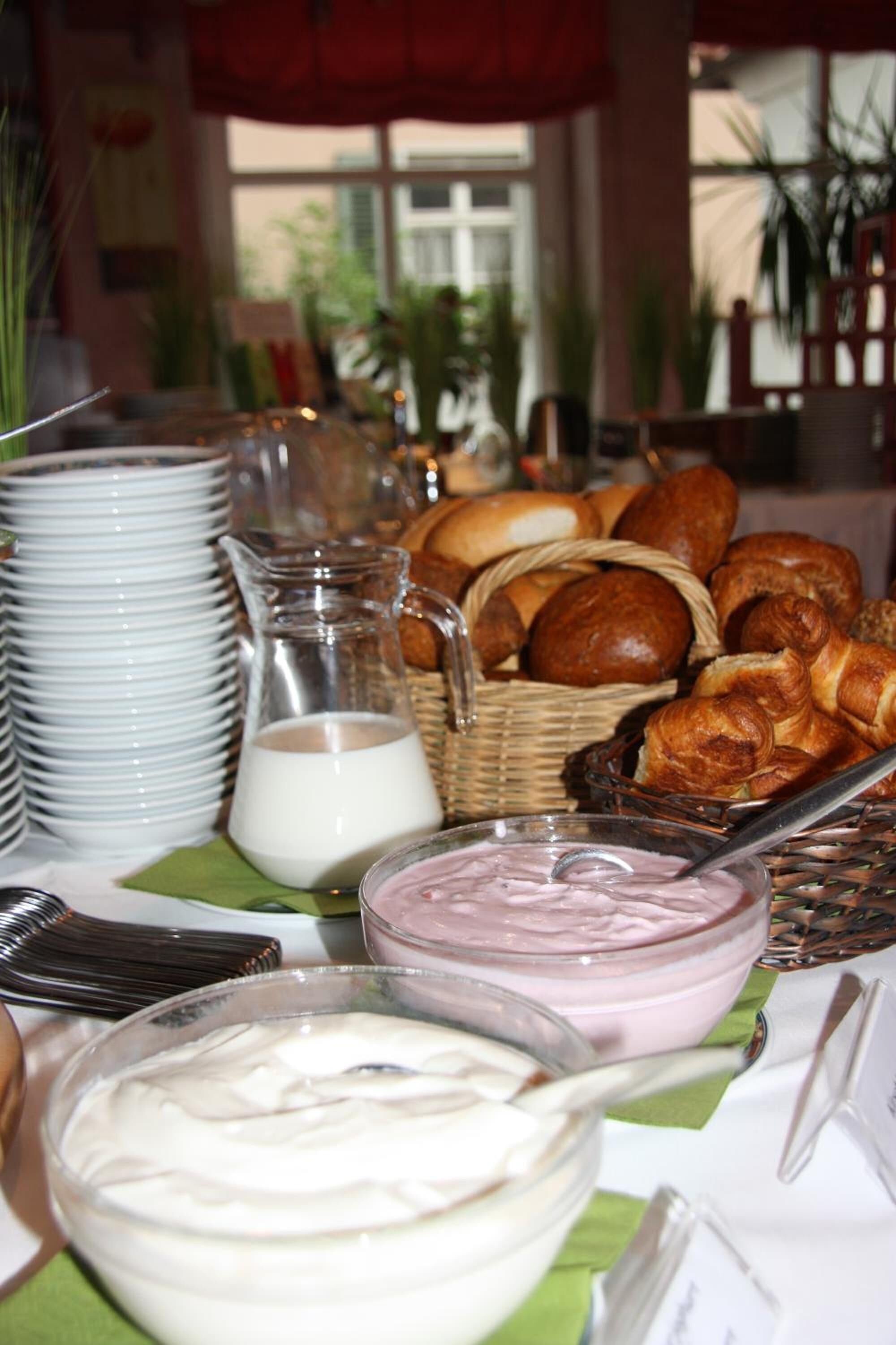 A breakfast buffet with various pastries, bowls of yogurt, and a pitcher of milk.