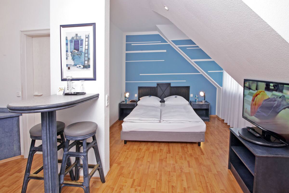 A modern bedroom with a bed, a desk with stools, a television, and a staircase.