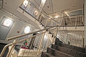 A multi-level interior with a staircase, handrails, and a small seating area with a flower arrangement. - Art Hotel Erlangen (Erlangen)