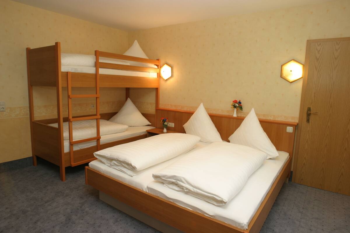 A hotel room with bunk beds, a wooden door, and a nightstand with a vase of flowers.
