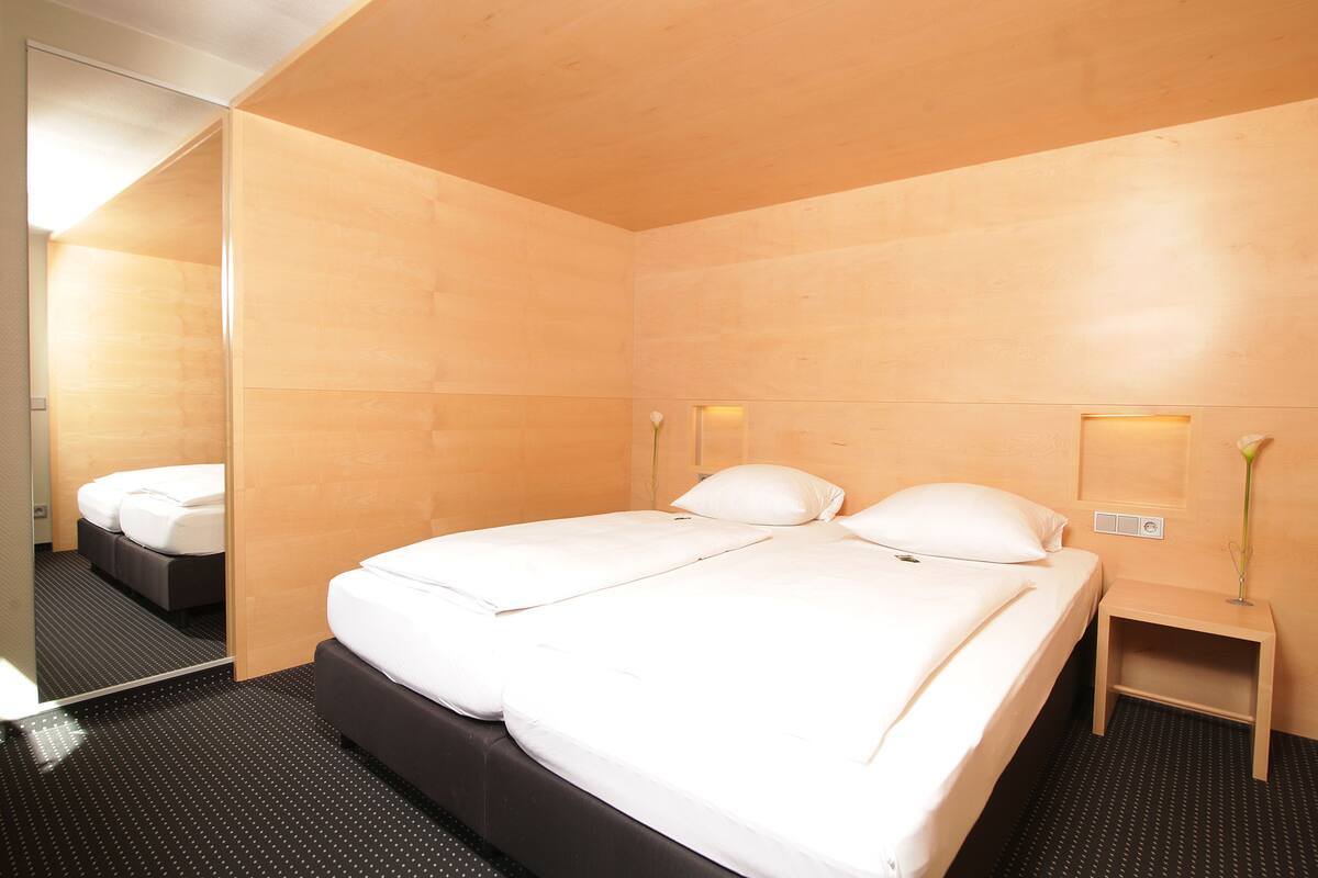 A modern hotel room with a large bed, a small bedside table, and a mirror.