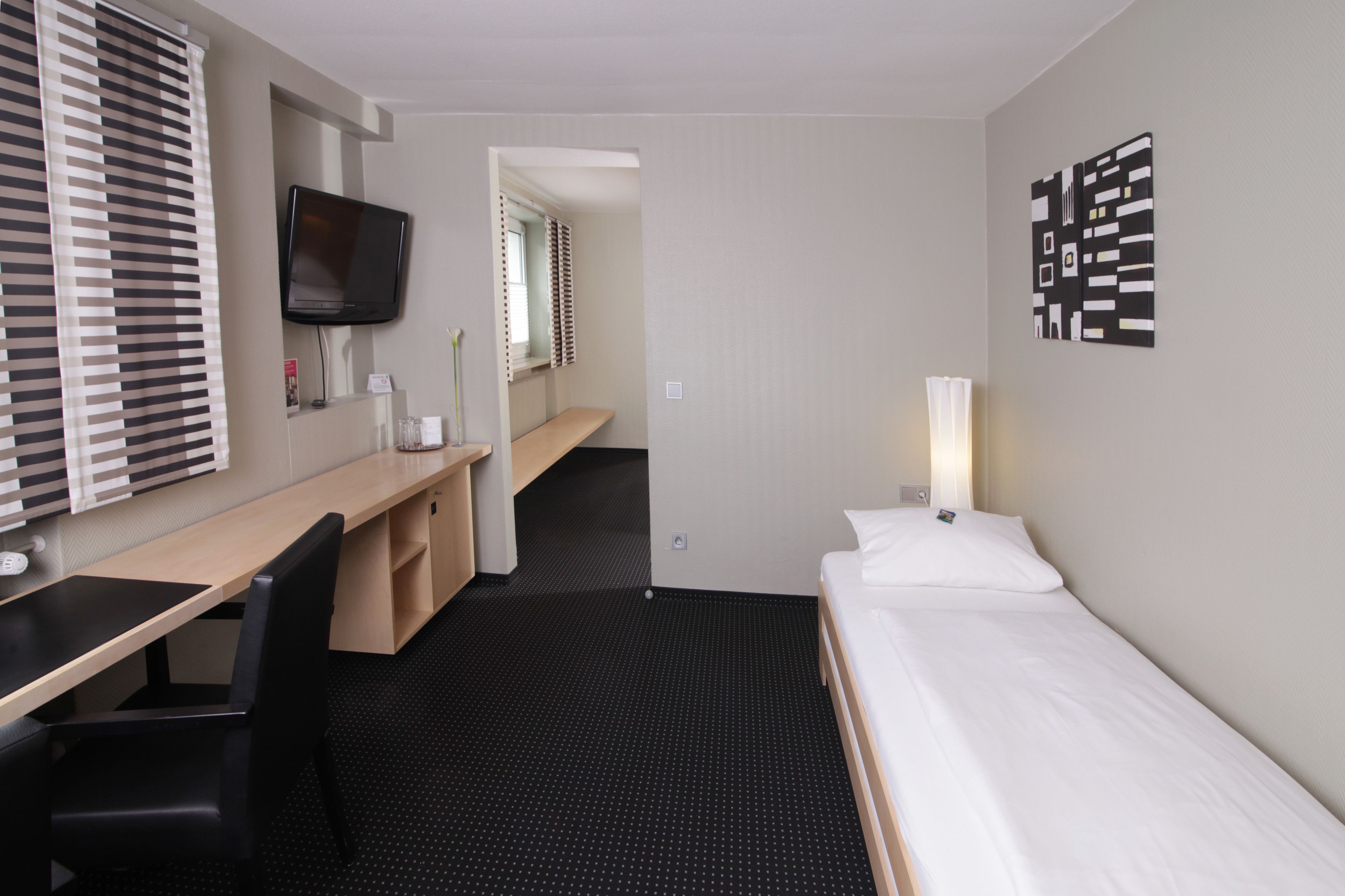 Une chambre d’hôtel équipée d’un lit, d’un bureau, d’une chaise, d’une télévision et d’une œuvre d’art accrochée au mur.