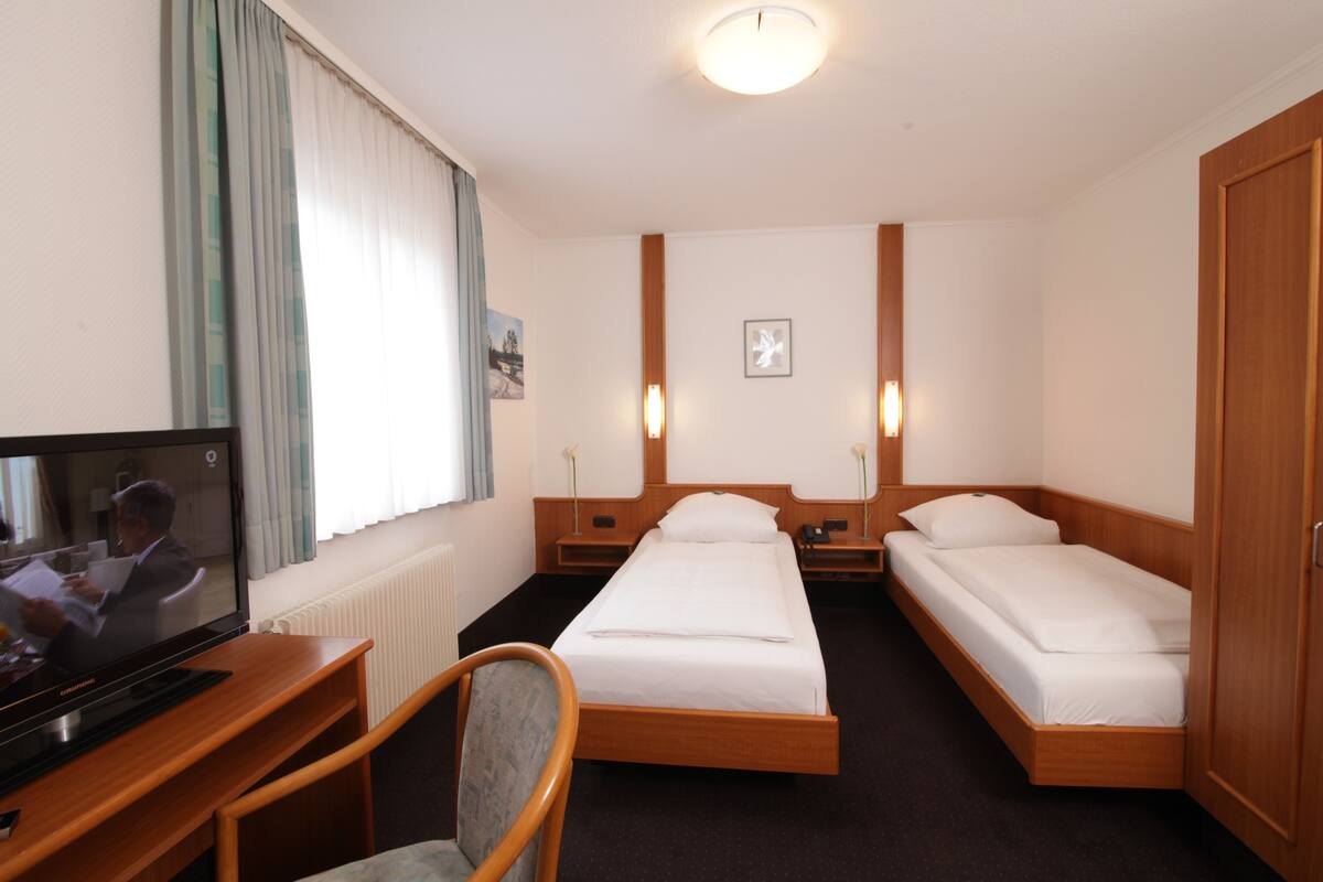 A hotel room with a bed, a desk with a television, and a chair.