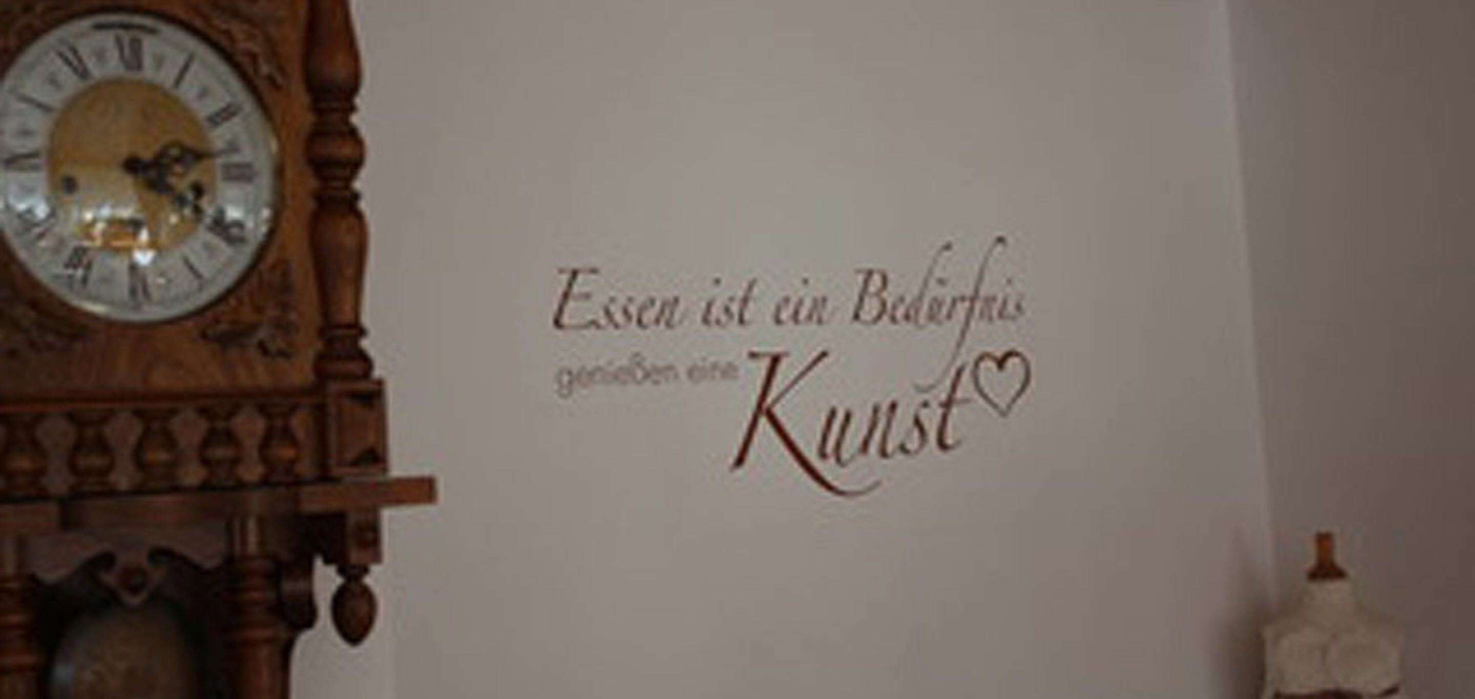 Eine Wand mit einer Uhr und einer dekorativen Aufschrift in Deutsch.