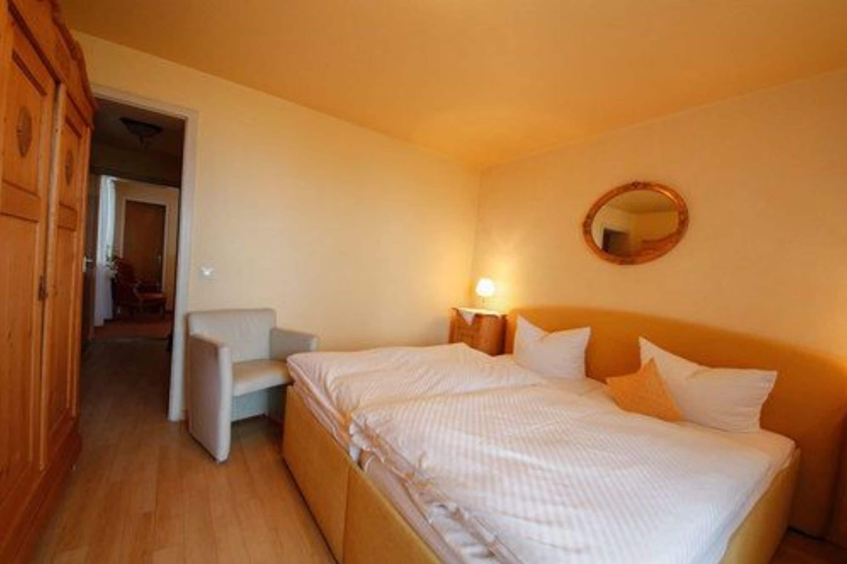 Ein Schlafzimmer mit Bett, Nachttisch mit Lampe, Stuhl und Spiegel an der Wand.