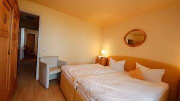 Ein Schlafzimmer mit Bett, Nachttisch mit Lampe, Stuhl und Spiegel an der Wand.