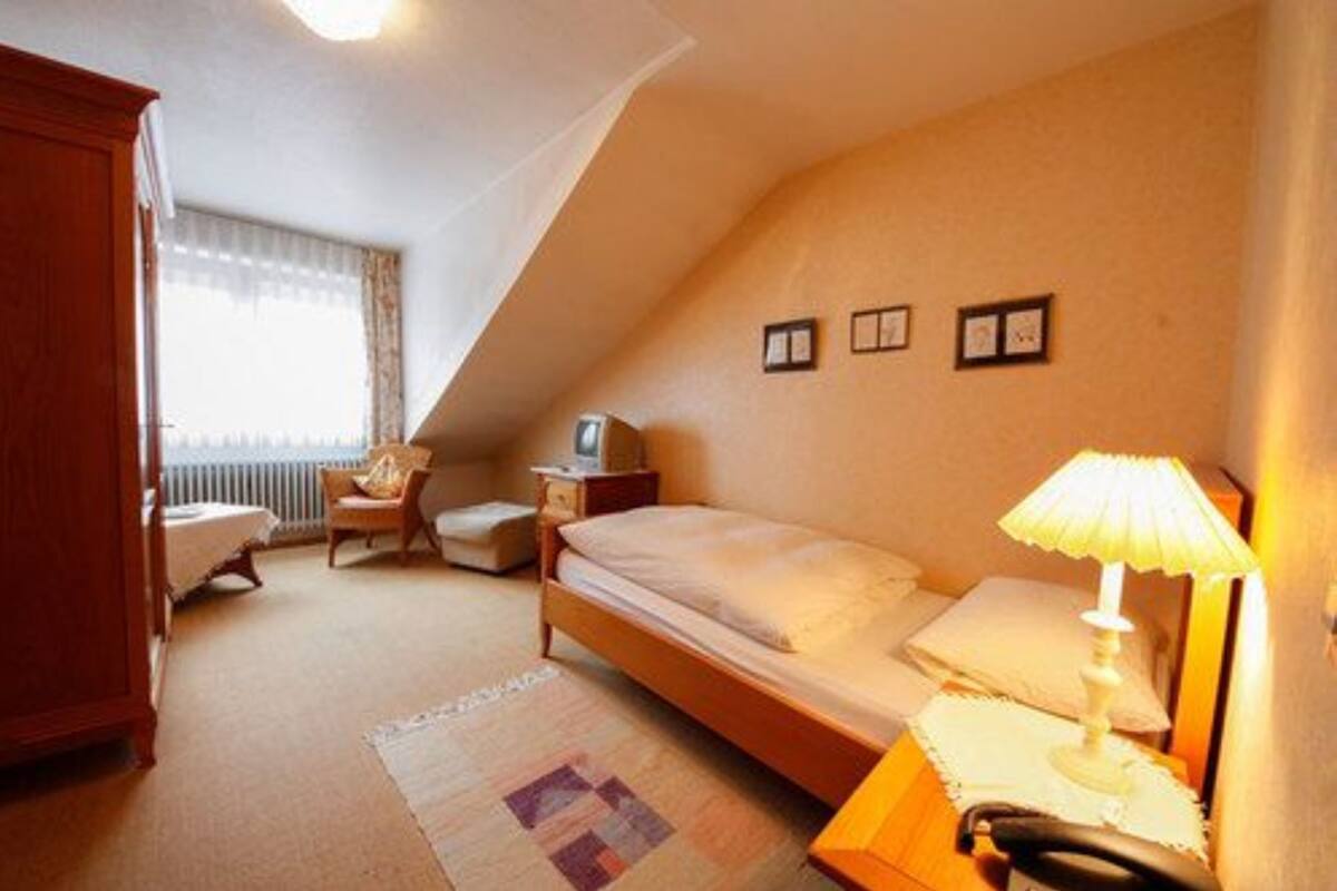 Un dormitorio con una cama individual, una mesita de noche, una lámpara, una silla y una ventana con cortinas.