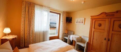 Una habitación de hotel con cama, escritorio, silla, armario y televisor en la pared.