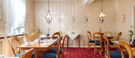 Un comedor con mesas y sillas de madera, una alfombra roja estampada y luminarias fijadas a la pared.