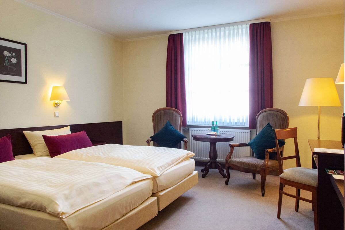 A hotel room with a large bed, two armchairs, a small table, and a desk with a lamp.