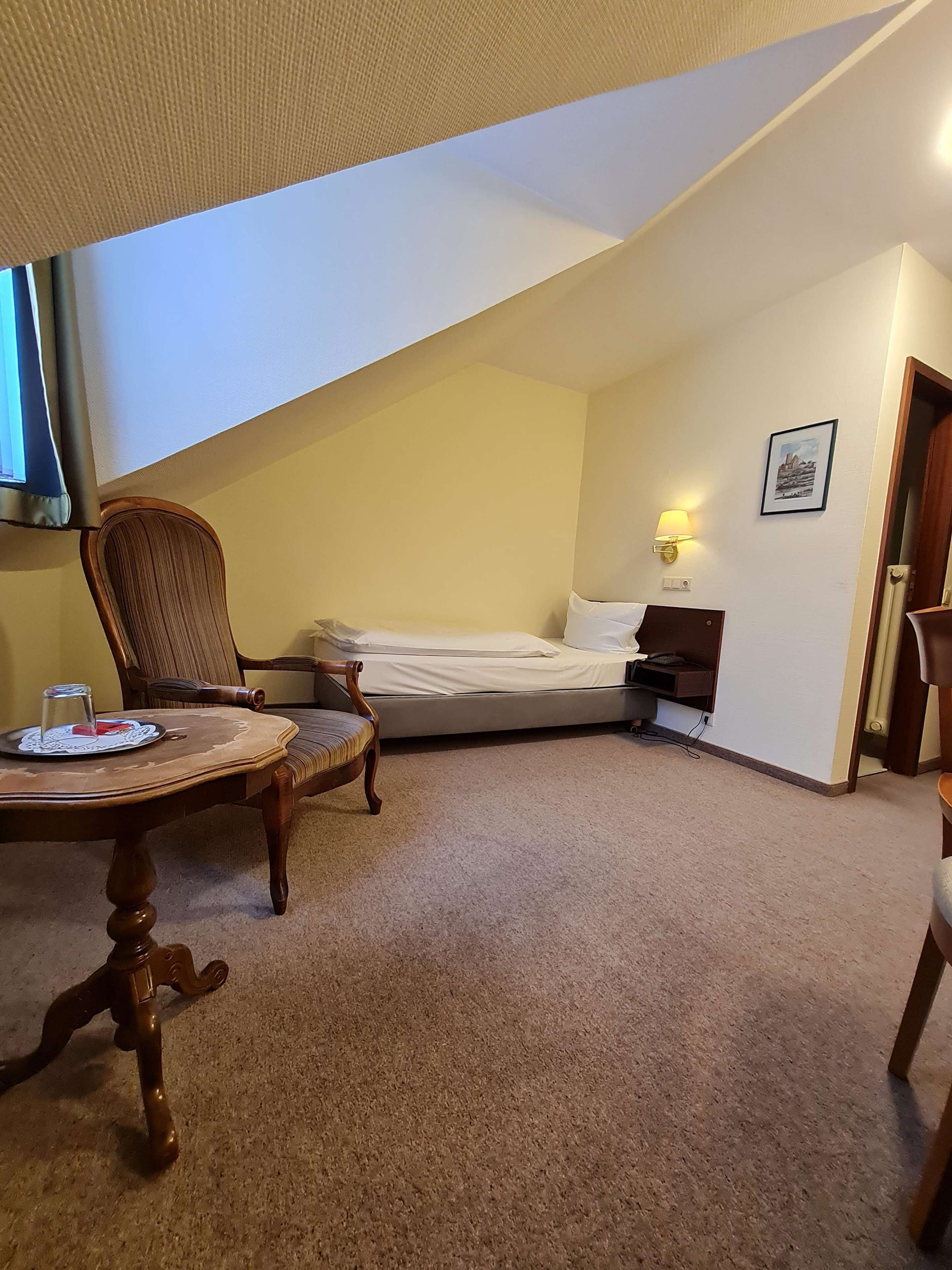 A small, cozy room with a bed, a chair, a table, and a lamp.