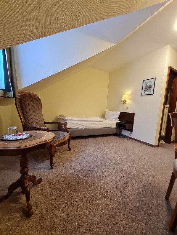 Una habitación pequeña y acogedora con cama, una silla, una mesa y una lámpara.
