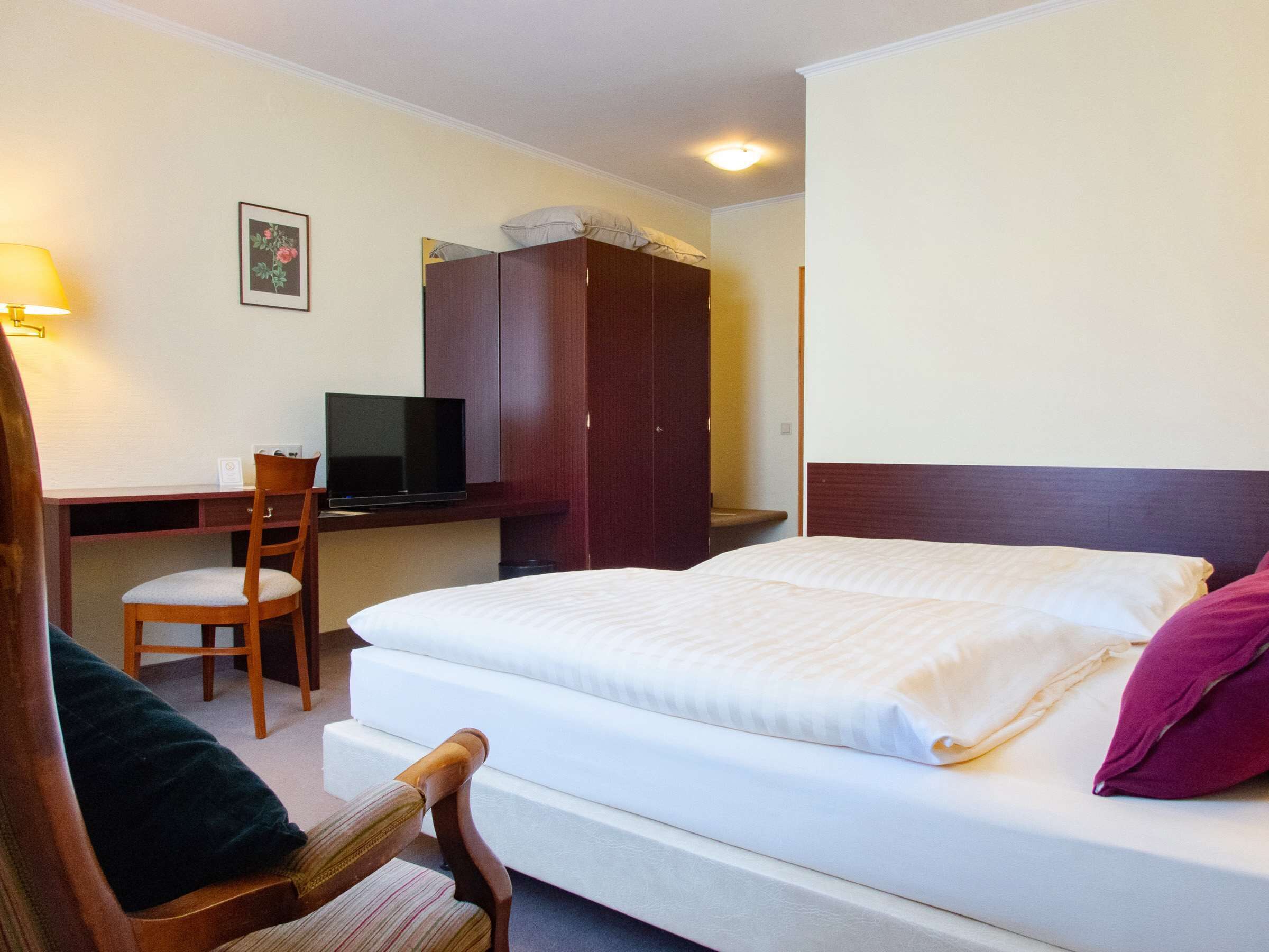 A hotel room with a bed, a desk with a television, a chair, and a wardrobe.