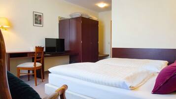 A hotel room with a bed, a desk with a television, a chair, and a wardrobe.