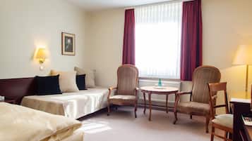 Quarto de hotel com duas camas de solteiro, um sofá, uma mesa pequena, duas poltronas e uma escrivaninha com abajur.
