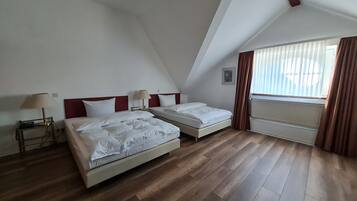 A room with two beds, a radiator, a window with curtains, and a lamp on a bedside table.