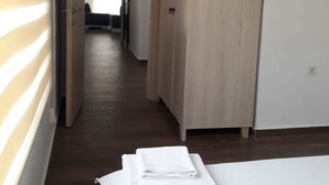 Une chambre d’hôtel avec une armoire en bois, un lit avec un matelas blanc et un couloir menant à une autre pièce.