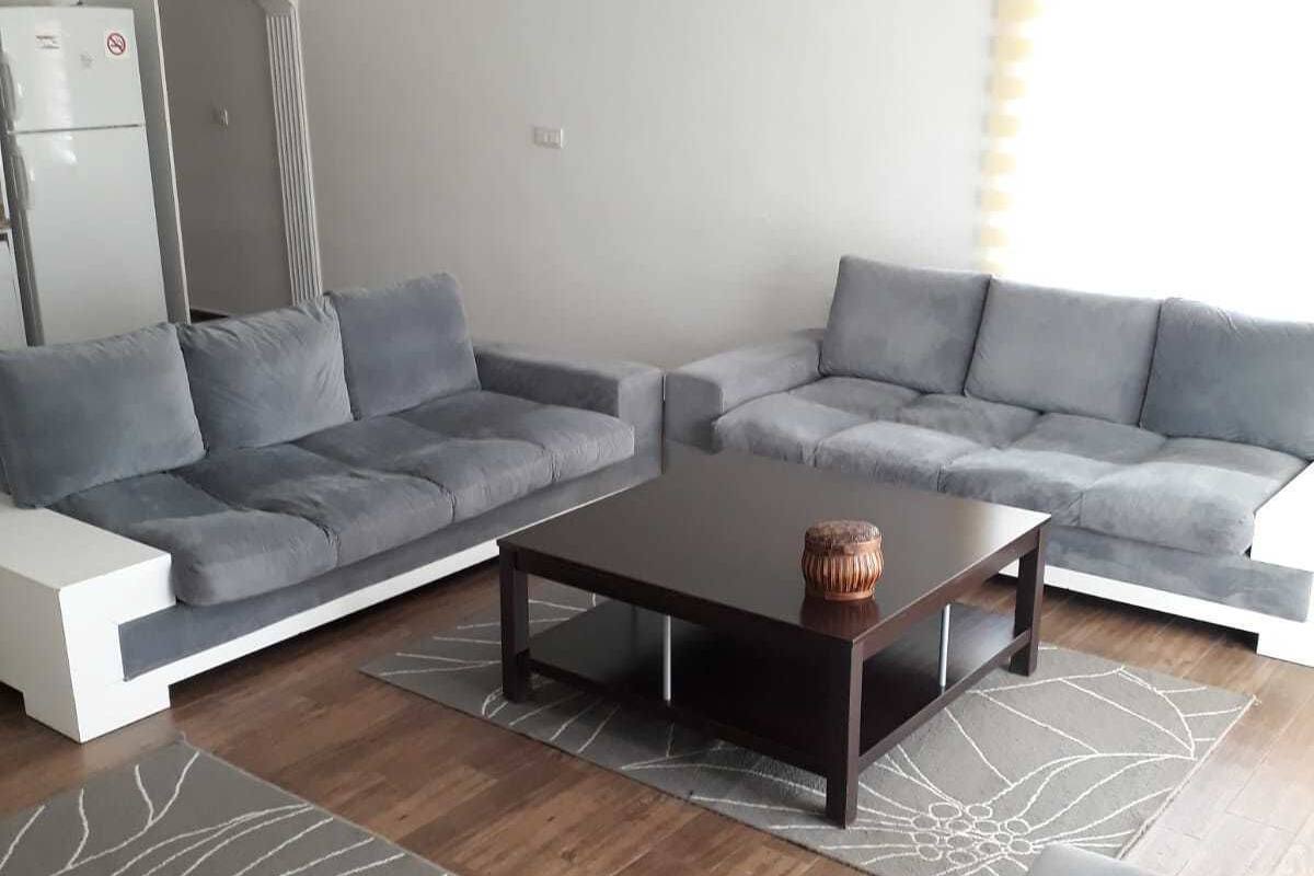 Ein modernes Wohnzimmer mit grauen Sofas, einem dunklen Couchtisch und einem gemusterten Teppich.