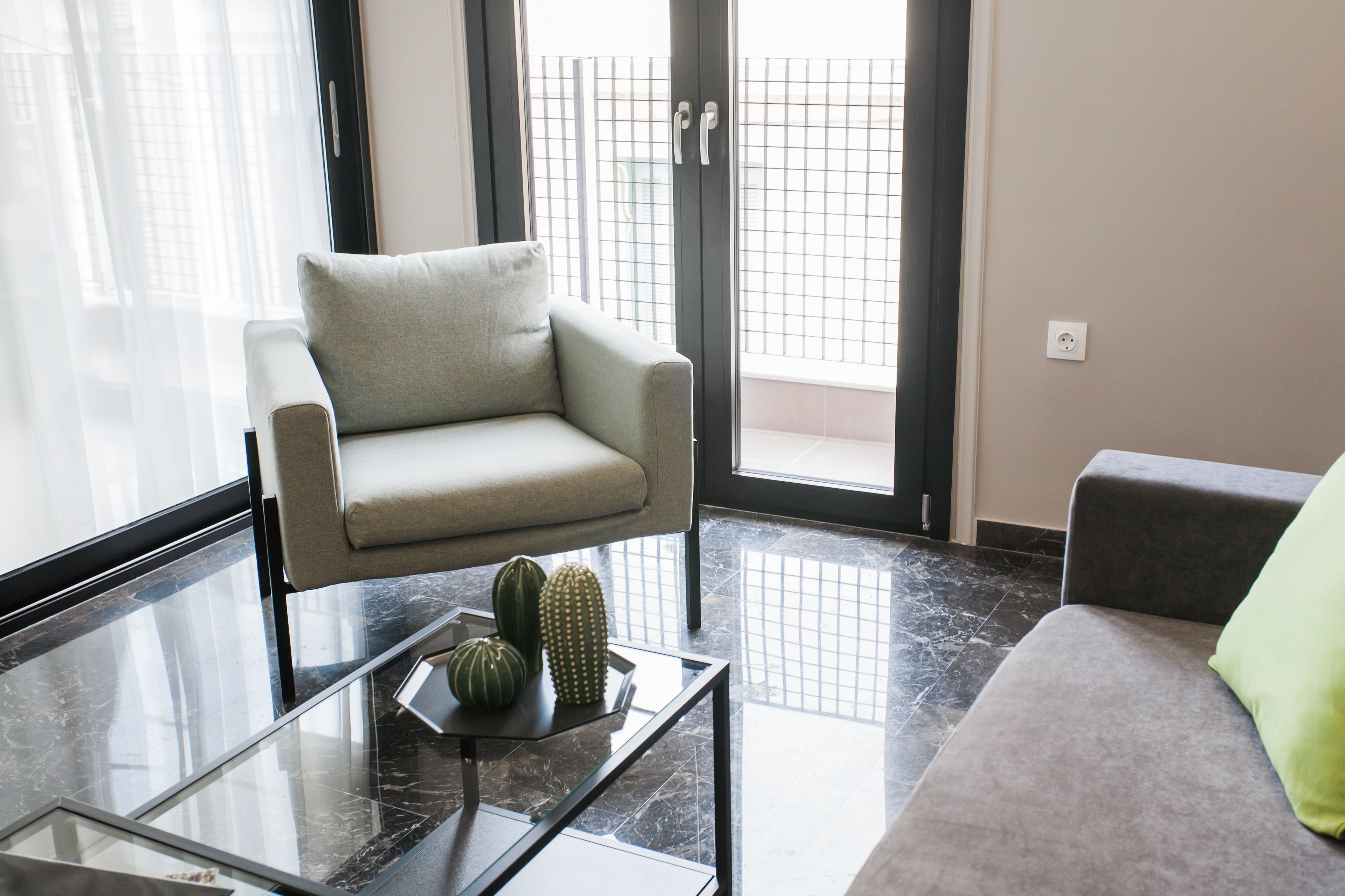 Ein modernes Wohnzimmer mit einem grauen Sofa, einem Glastisch mit Dekoration und Blick durch eine Glastür.