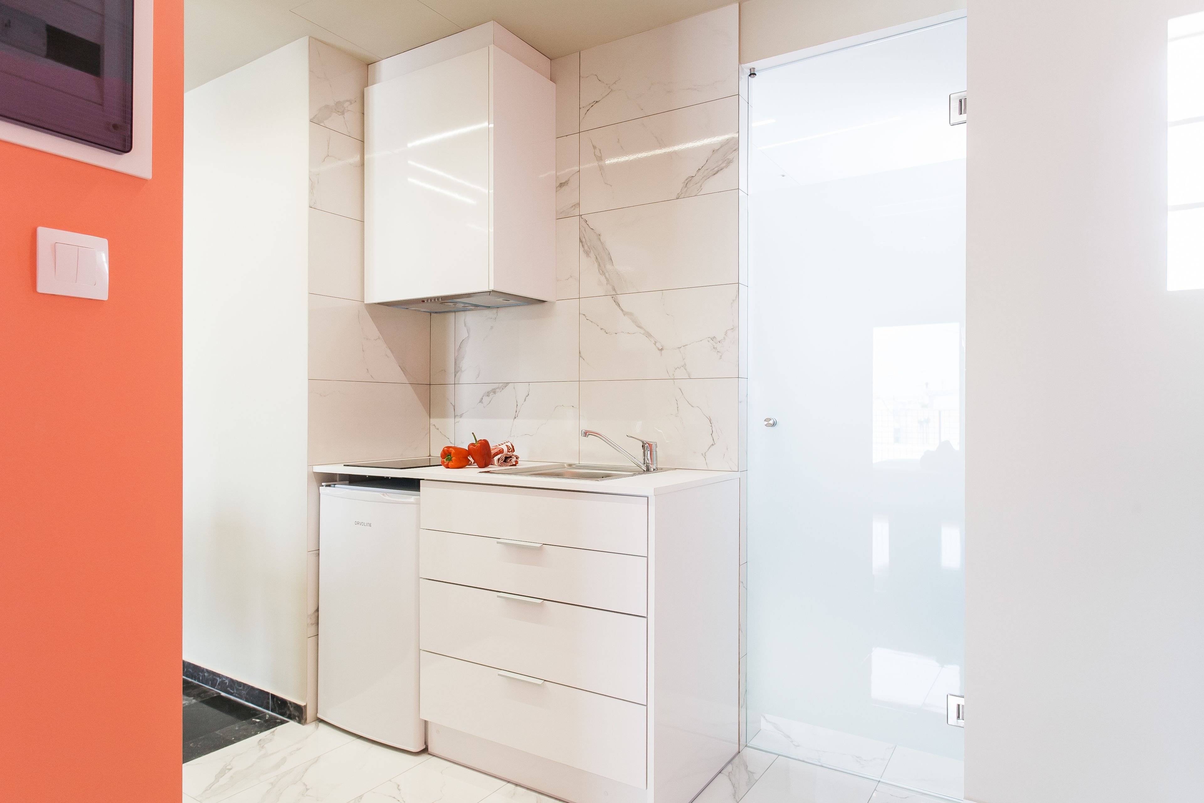 A modern kitchen with white cabinetry, a built-in oven, and a marble backsplash.