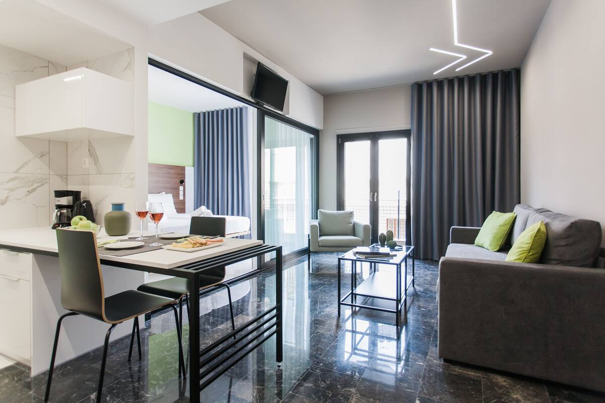 Una sala moderna con un sofá, un comedor con una mesa y sillas, y una cocina con mostrador y electrodomésticos.