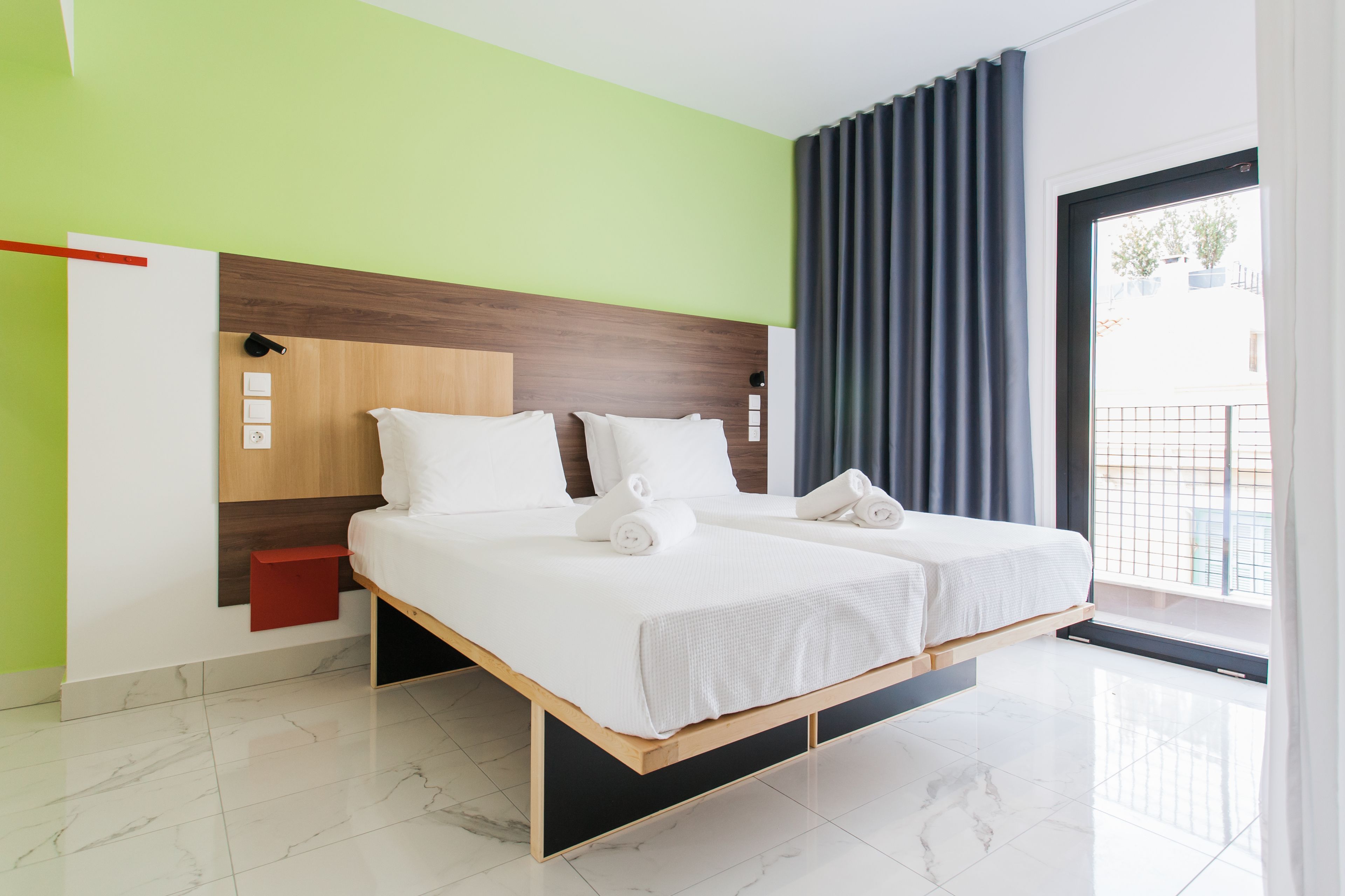 Ett modernt hotellrum med en stor säng, en sänggavel i trä och utsikt över omgivningarna genom ett stort fönster.
