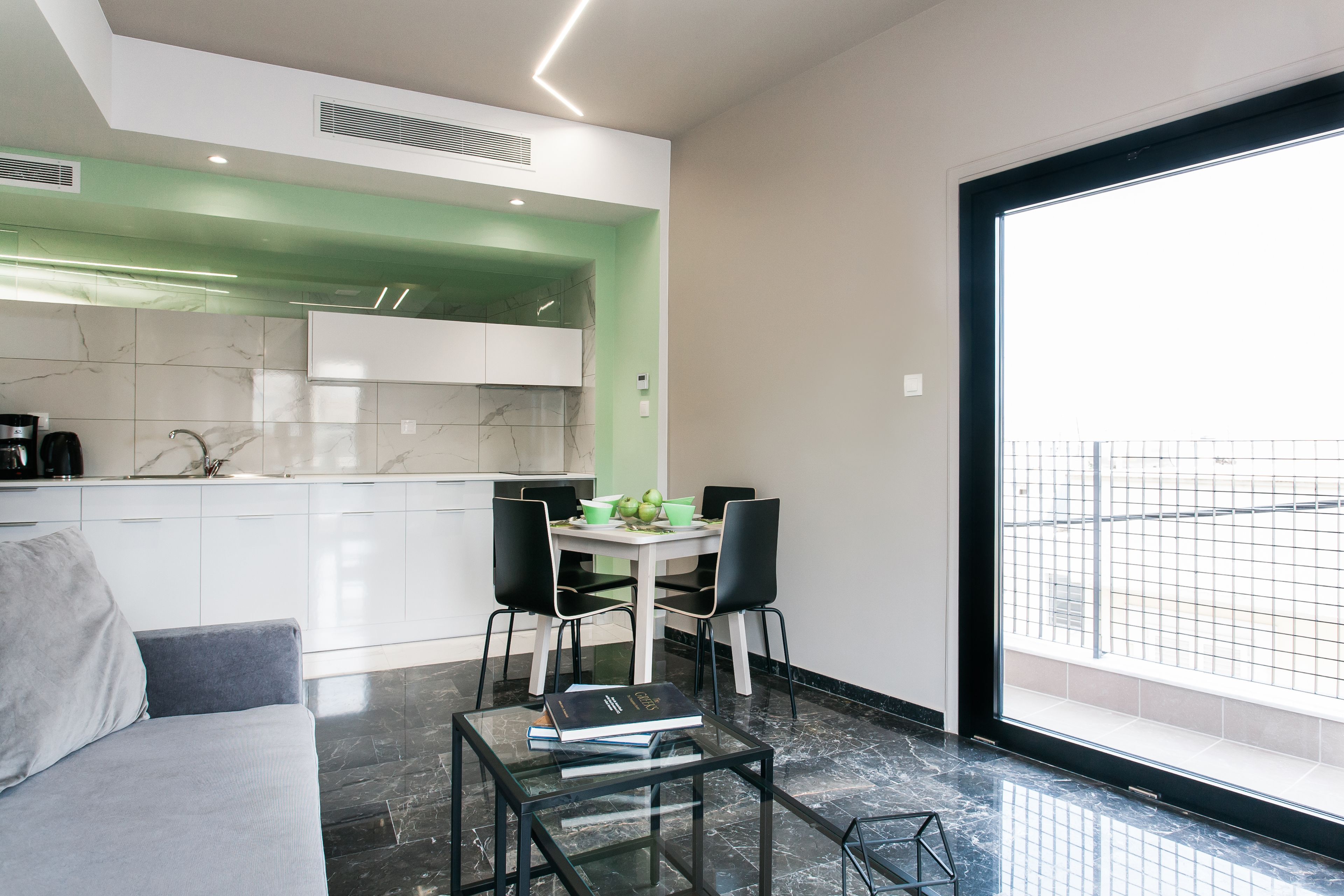 A modern kitchen with white cabinets, a green accent wall, and a dining area with a table and chairs.