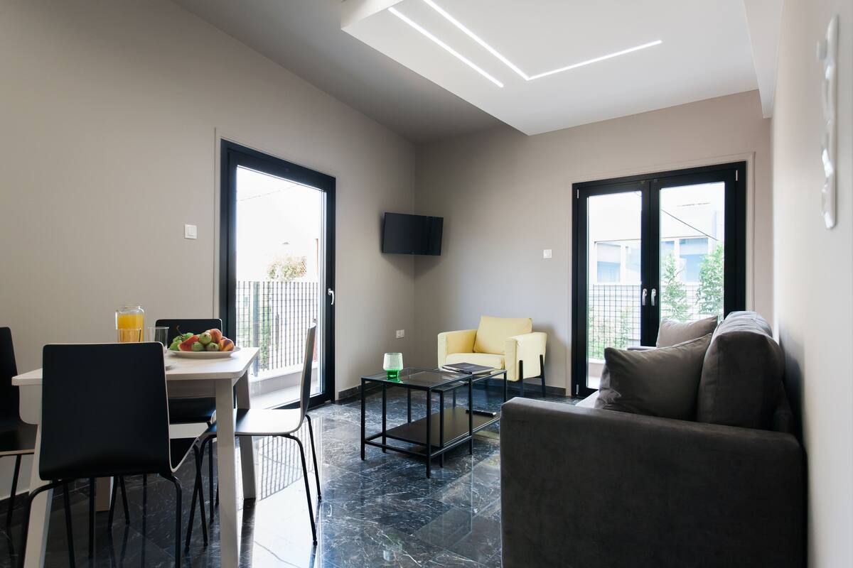 Una sala de estar moderna con un sofá, una mesa de comedor con sillas, una mesa de centro y un televisor montado en la pared.