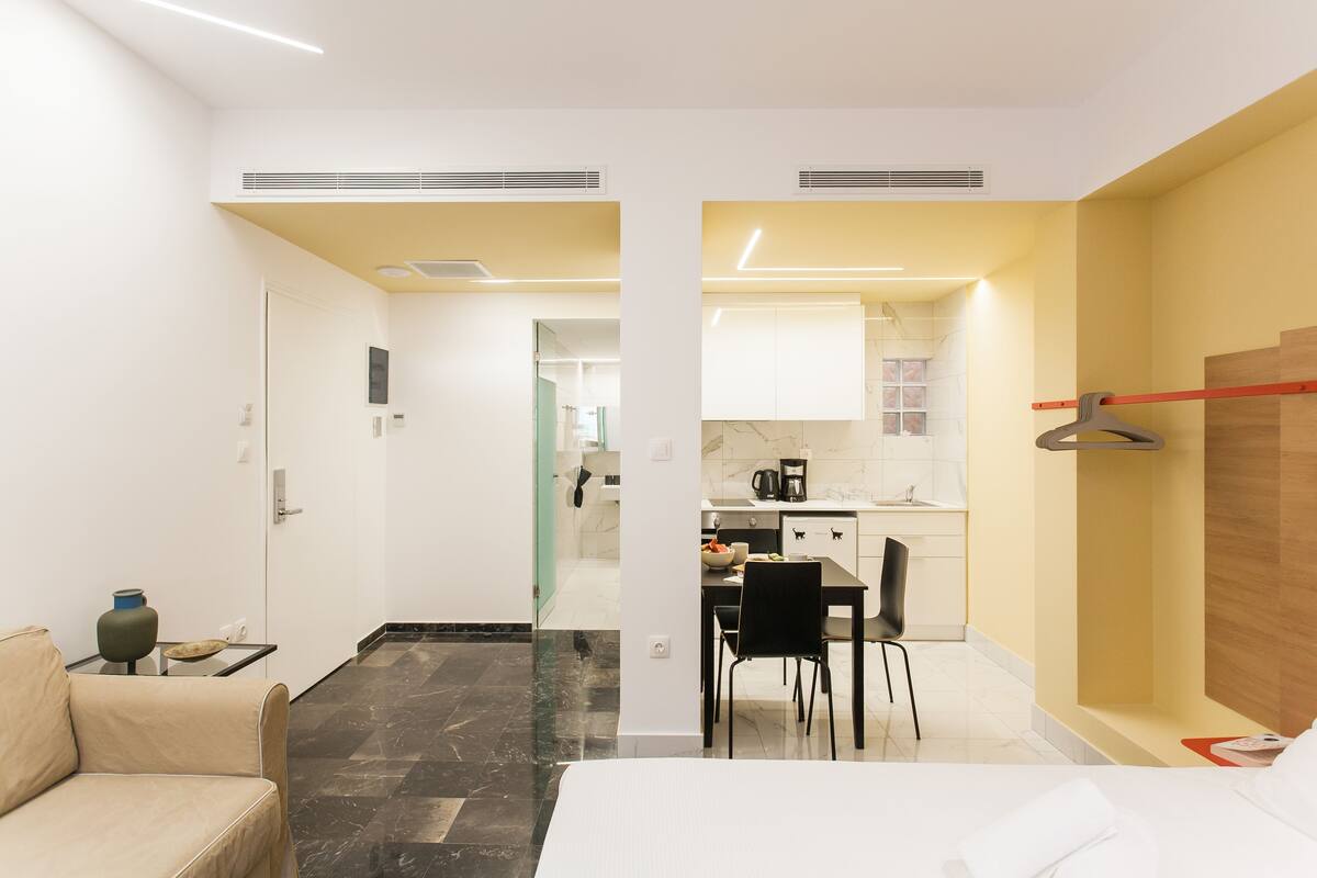 Una habitación de hotel moderna con cama, una pequeña zona de estar, una mesa de comedor con sillas y una kitchenette.