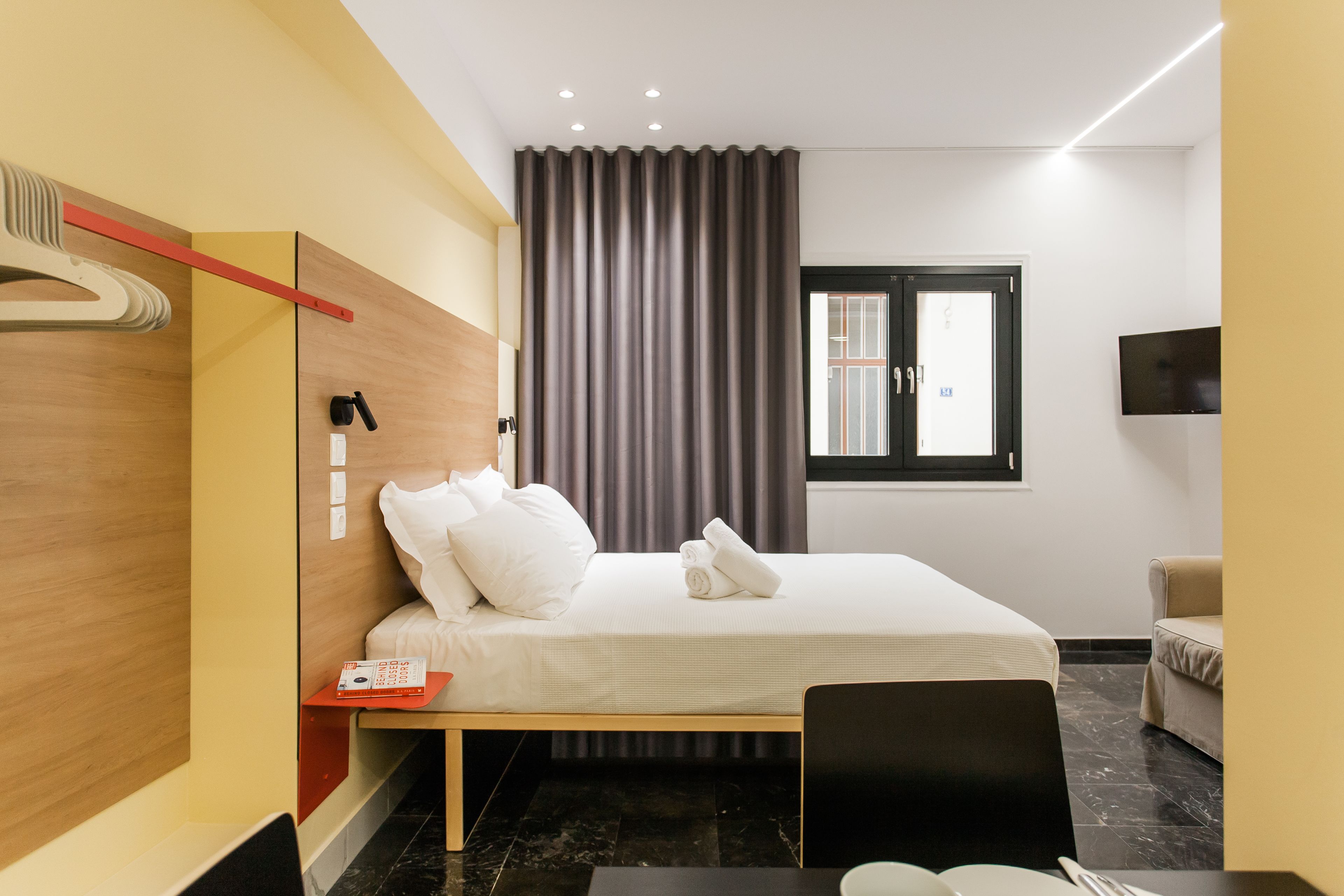 A modern hotel room with a neatly made bed, a flat-screen TV mounted on the wall, and a window with a view of the outside.