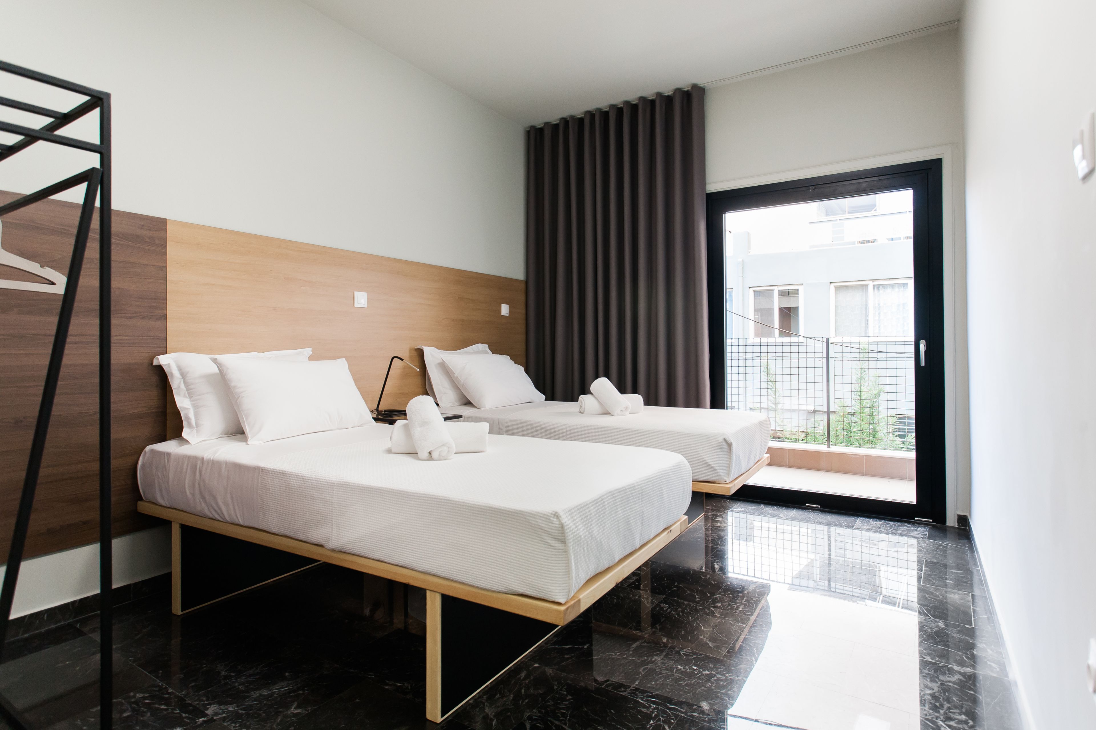 A hotel room with two beds, a wooden headboard, a balcony with curtains, and a modern design.