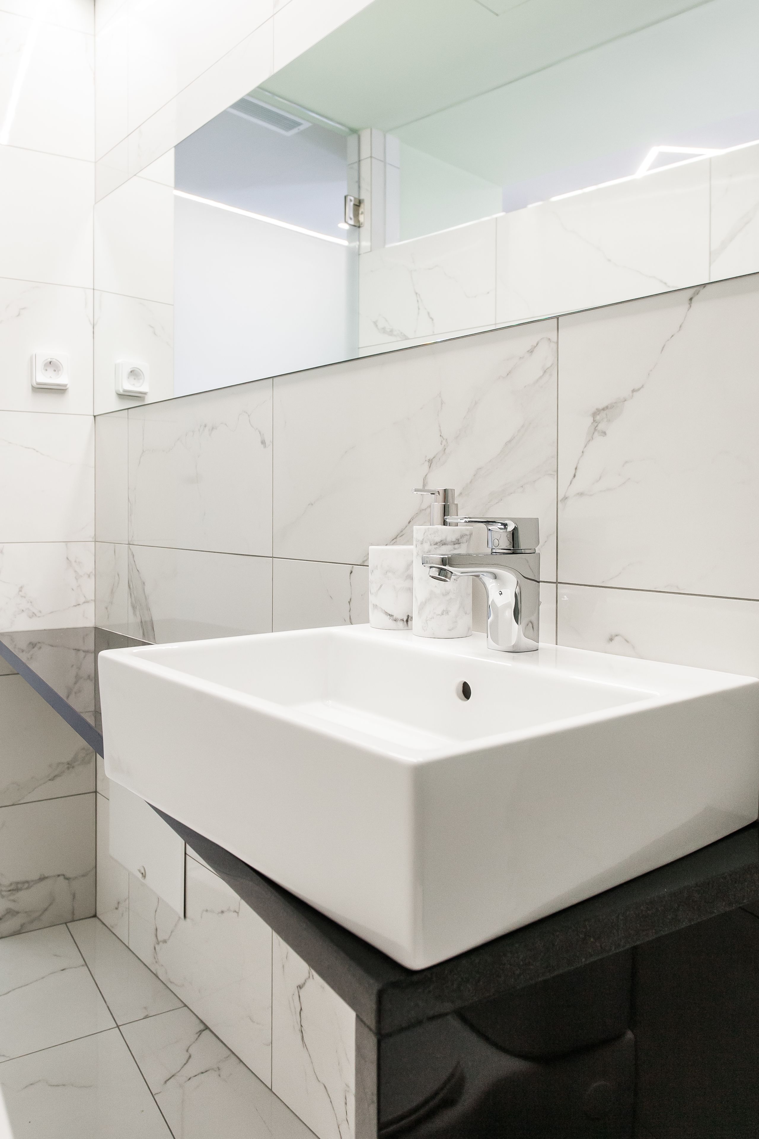 A modern bathroom with a large white sink, chrome faucet, and marble tiles.