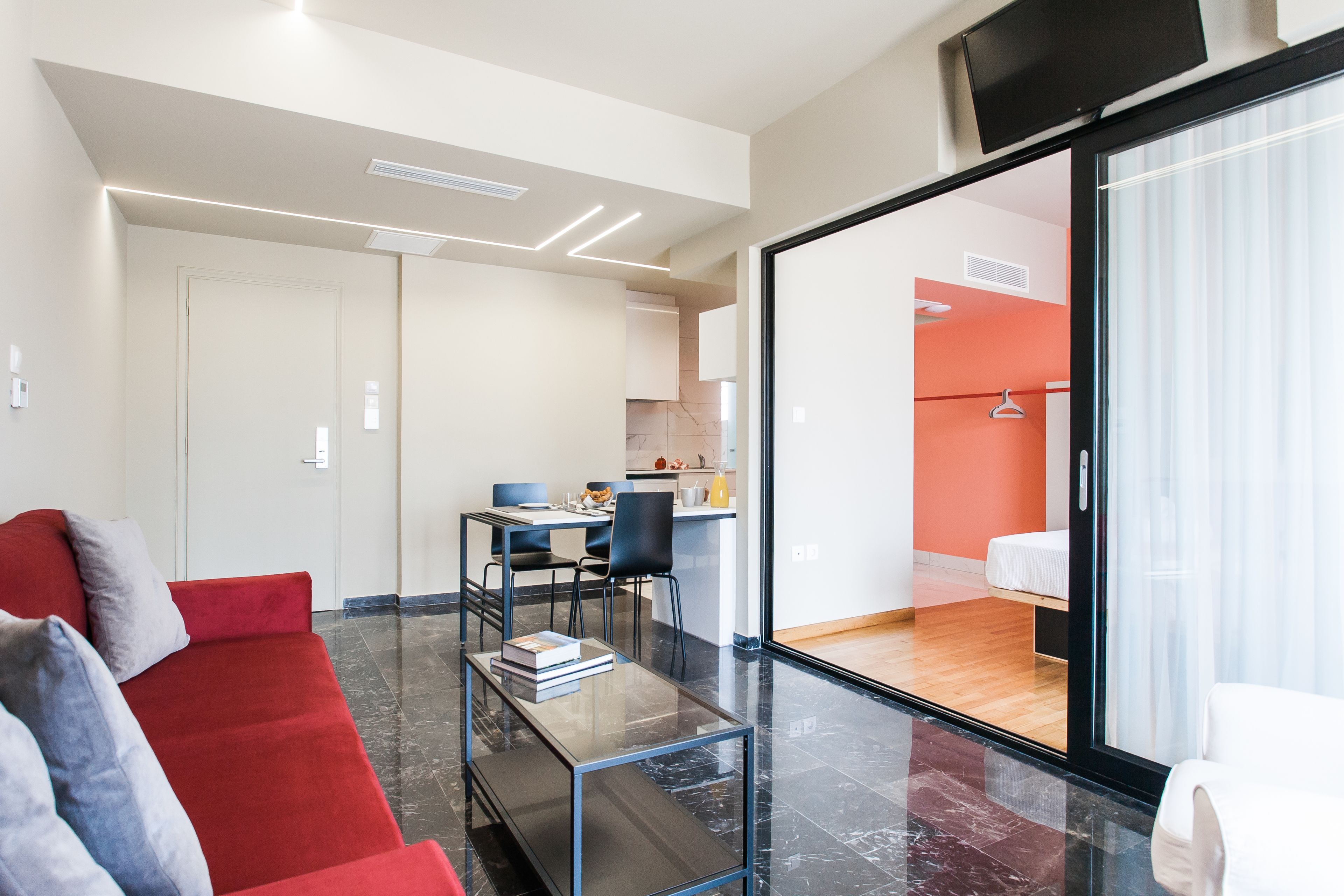 Un salon moderne avec un canapé rouge, une table basse en verre et un coin repas comprenant une table et des chaises.