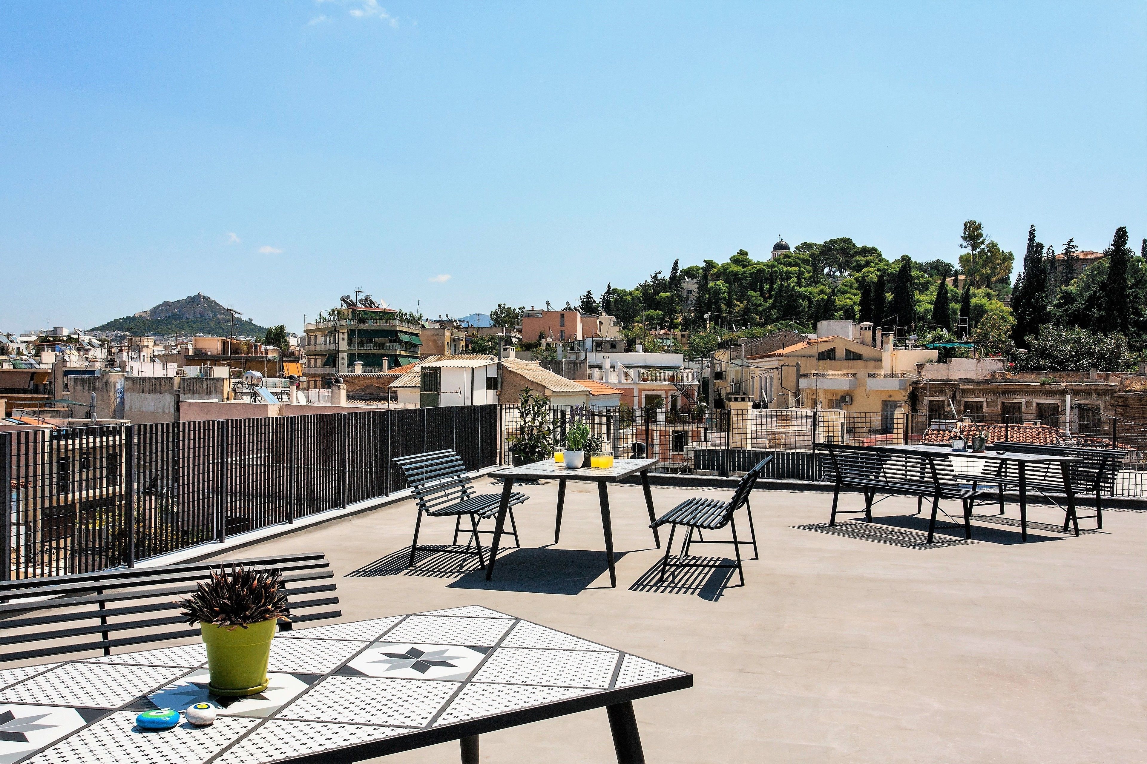 A rooftop terrace with a table and chairs, a potted plant, and a view of the cityscape and a hill in the distance.