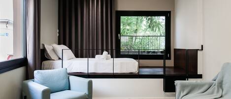A modern hotel room with a bed, a sofa, a coffee table, and a large window with a view of greenery.