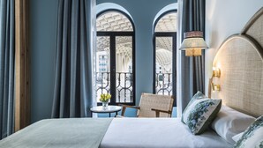 A hotel room with a large bed, two chairs, a small table with flowers, and a view through arched windows. - Intelier Casa de Indias Hotel by Intelier Hotels & Suites (Seville)