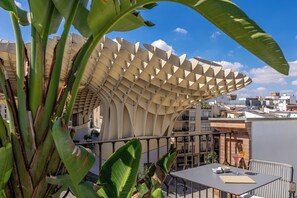 A modern building with a unique geometric roof structure, surrounded by urban buildings and greenery.