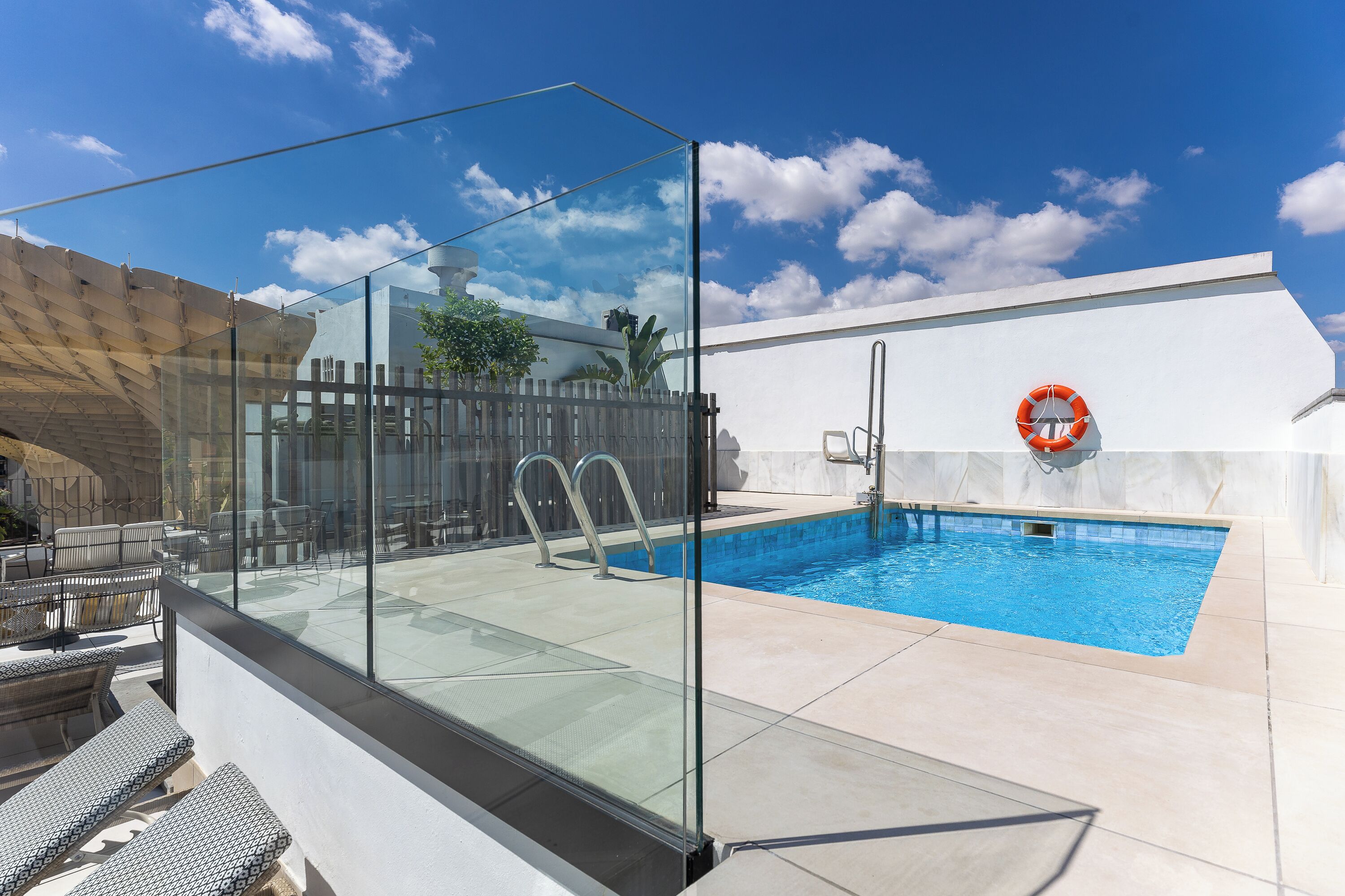 Una piscina en la azotea con barandillas de cristal, un flotador salvavidas y mobiliario de exterior.